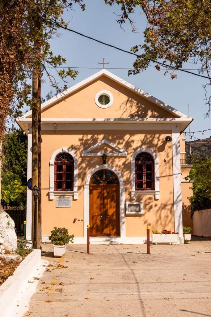 She Knows Alt Text said:

Front view of a small peach-colored church in Assos, Kefalonia, with arched red-trimmed windows and a wooden central door framed by white architectural details. A simple cross tops the triangular pediment, and the sun casts tree shadows across the facade, adding to the peaceful village setting.