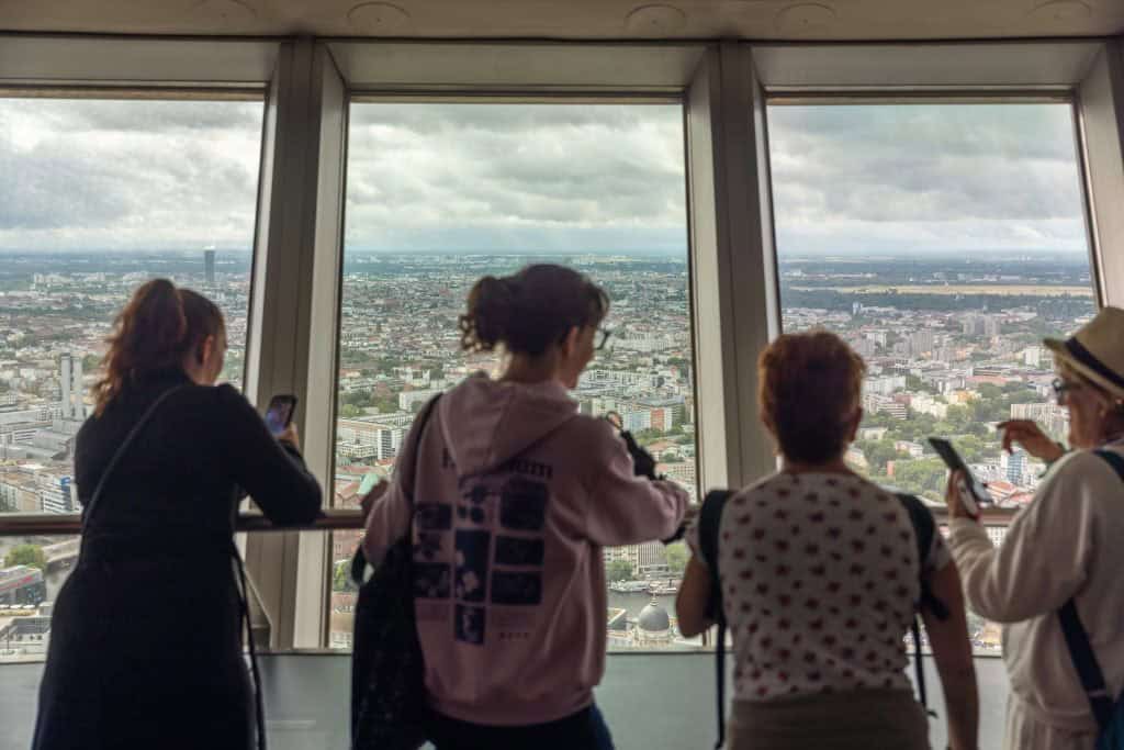 Group of visitors taking photos of Berlin's skyline through the observation deck windows of the TV Tower.
