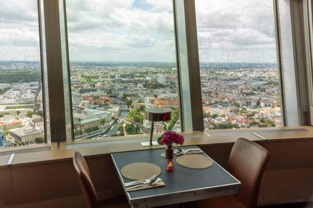 Set restaurant table for two beside floor-to-ceiling windows in the Berlin TV Tower, overlooking the Spree River and city rooftops below.